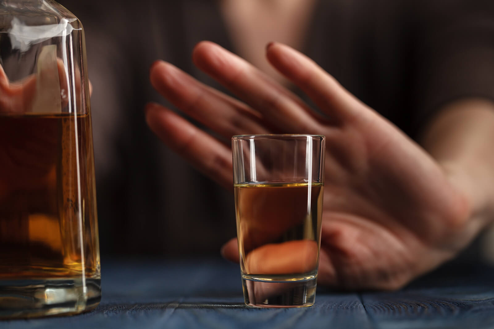 Hand pushing away a glass of whiskey in an attempt to remain sober.